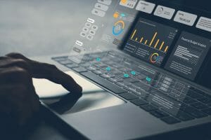 Close-up of a person's hand interacting with a laptop displaying various data analytics graphs and charts on the screen, essential for crafting an effective marketing strategy.