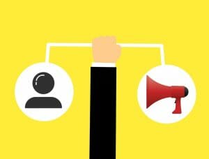Illustration with a hand holding a balance scale. One side has a user icon, and the other side has a red megaphone, symbolizing local marketing strategies, set against a yellow background.